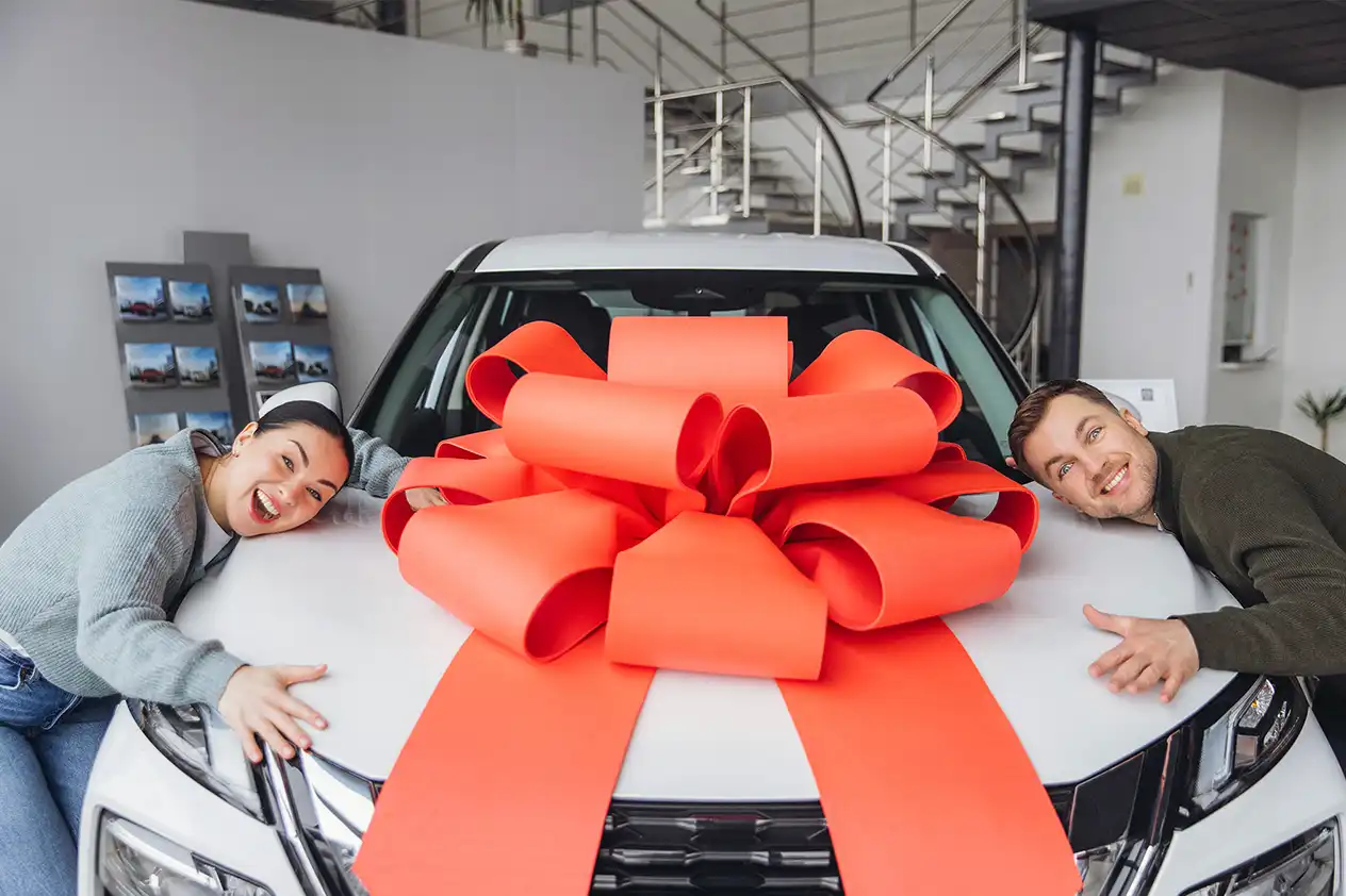 A couple celebrating their new vehicle wrapped in a red bow